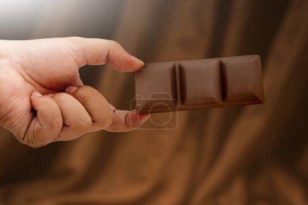 Foto de Close up human hand holding chocolate bar, concept of giving on world chocolate day. Sweet and energy snack. Mock up deisign. - Imagen libre de derechos