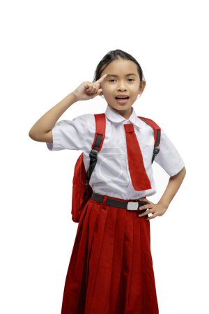 Junges asiatisches Mädchen in weißem Hemd und rotem Rock mit Schuluniform salutiert selbstbewusst und enthusiastisch vor weißem Hintergrund