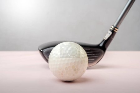 Closeup of a golf ball aligned with a driver on a soft pink background, presenting a clean and minimalist look for sports and leisure themes