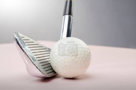 Fotografía macro que muestra una vista detallada de una pelota de golf junto a una plancha de golf con un fondo gris softfocus, destacando texturas y equipos utilizados en el deporte