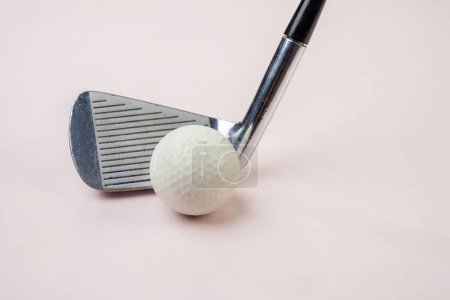 Closeup image of a golf club and white golf ball against a soft pink background, depicting a minimalist and modern approach to sports equipment presentation