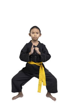 Focused young child demonstrates a karate stance, wearing a black gi with a yellow belt, symbolizing an intermediate level, isolated on a white background, showcasing discipline and strength