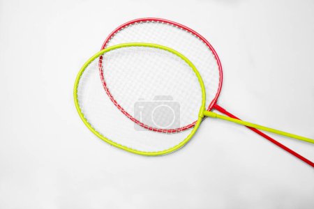 Zwei Badmintonschläger mit leuchtend roten und gelben Rahmen kreuzten sich vor einem weißen Hintergrund, der die Ausrüstung für den schnelllebigen Schlägersport darstellt.