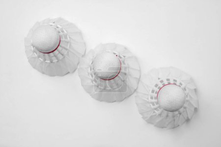 Three white badminton shuttlecocks with red details arranged neatly on a white surface, creating a minimalist design suitable for sportrelated articles and promotional materials