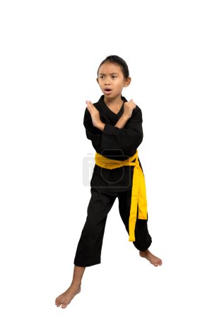 Focalisée jeune fille dans un gi de karaté noir avec une ceinture jaune se tient dans une position défensive des arts martiaux, démontrant la discipline et la force sur un fond blanc