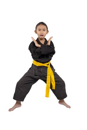 Focused young girl in a black karate gi with a yellow belt demonstrating a defensive stance against a white background, ready for martial arts training or competition