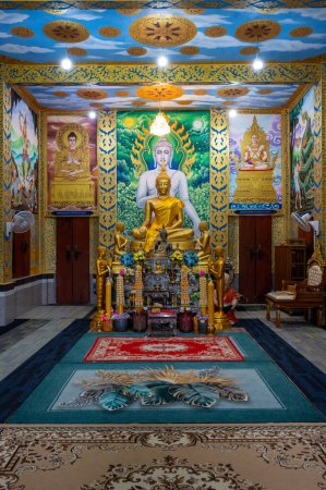 Photo for Chachoengsao, Thailand, 28 July 2023. Wat Khao Tham Raet, Golden Buddha statue sitting in a temple. The statue is seated on a red rug and has its eyes closed. Behind the statue is a mural on the wall. The mural is painted in bright colors and has a l - Royalty Free Image