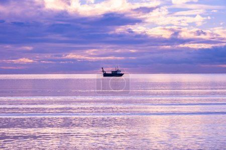 Téléchargez les photos : A cold day in Troon Scotland as the sun starts to go down behind the horizon and a loan fishing boat in the Bay with its nets stretched out on either side. - en image libre de droit