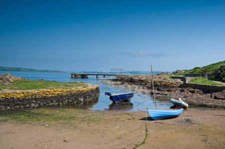 Photo for Looking over the rocky harbour  to the old jetty and some small boats at Portencross in Seamill West Kilbride on a bright summers day in June with blue sky and Cumbrae in the distance. - Royalty Free Image