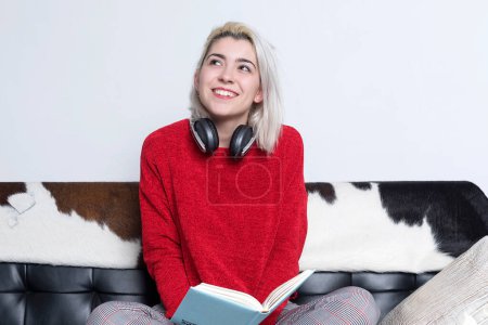 Foto de Una joven atractiva que pasa tiempo en casa. Acostado en un sofá con libro - Imagen libre de derechos