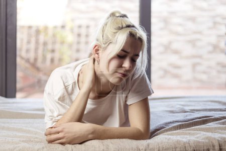 Upset young woman lying in bed in morning feels pain in neck after night sleep