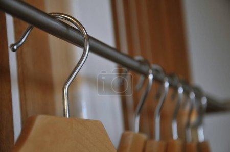 Photo for Modern wooden wardrobe with clothes hanging on rail in walk in closet, Choice of fashion clothes of different colors on wooden hangers - Royalty Free Image