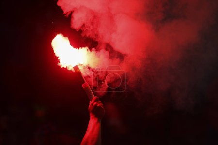 Détails avec les mains d'un homme tenant une torche à l'intérieur pendant un match de football.