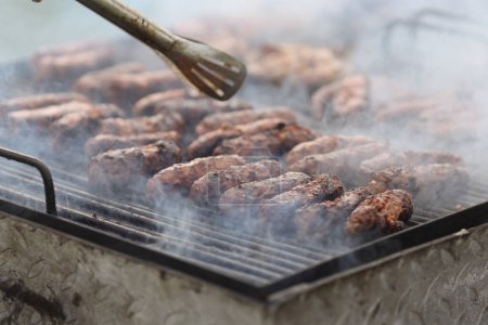 Shallow depth of field (selective focus) details with Romanian traditional mici (mititei), grilled ground meat rolls in cylindrical shape on the barbecue grill.