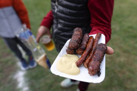 Téléchargez les photos : Personne tenant à la main des mici traditionnels roumains (mititei), des rouleaux de viande hachée grillés en forme cylindrique, des susages et de la moutarde. - en image libre de droit