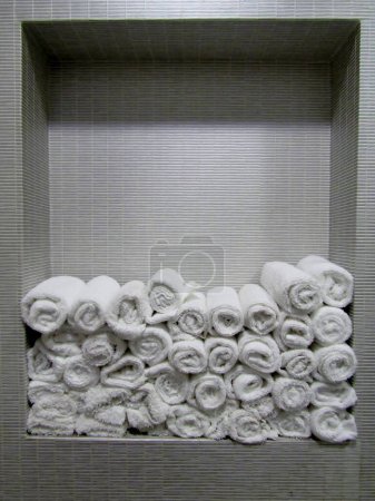 Photo for Rolled white soft hand towels on tile built in shelf in restroom - Royalty Free Image
