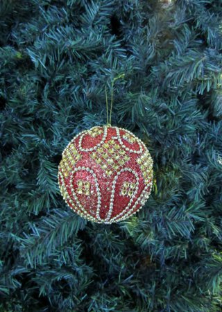 Red glitter beaded Christmas ball hanging on green tree