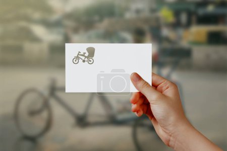 Photo for Man's hand holding Cycle Rickshaw symbol paper on road. Concept of journey, travel, dream, freedom. Hand is holding paper Cycle Rickshaw against road with empty space for text. - Royalty Free Image