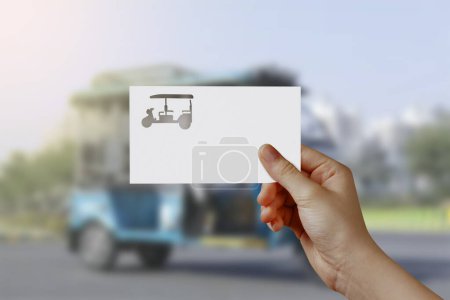 Photo for Man's hand holding Electric Rickshaw symbol paper on road. Concept of journey, travel, dream, freedom. Hand is holding paper Battery Rickshaw against road with empty space for text. - Royalty Free Image