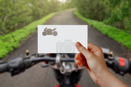 Photo for Man's hand holding bike symbol paper on road. Concept of journey, travel, dream, freedom. Hand is holding paper bike against road seated on bike with empty space for text. - Royalty Free Image