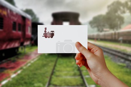 Photo for Man's hand holding train symbol paper on railway station. Concept of journey, travel, dream, freedom. Hand is holding paper train against rail road with empty space for text. - Royalty Free Image