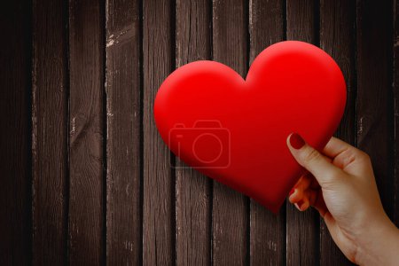Téléchargez les photos : Valentines week special illustration idea. Man's hand holding a heart on dark wooden background. Empty Space. - en image libre de droit