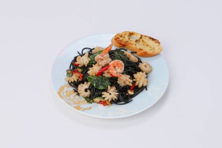 Téléchargez les photos : Pâtes noires - Encre de calmar, avec crevettes, calmar, chili et basilic dans un bol blanc sur fond isolé. - en image libre de droit