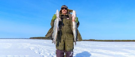 Téléchargez les photos : Homme tenant un brochet de poisson dans la neige. Pêche d'hiver, aventure. Bannière, espace de copie - en image libre de droit