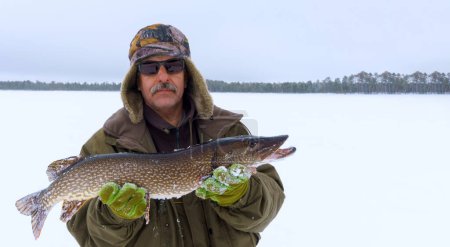 Téléchargez les photos : Un homme tenant un poisson dans la neige. Pêche d'hiver, aventure. Bannière, espace de copie - en image libre de droit