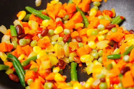 Cuillère agite vigoureusement un mélange de légumes dans une casserole pétillante, créant une symphonie de couleurs et d'arômes.