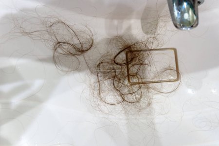 Un gros plan révèle un évier recouvert de mèches de cheveux. Restes emmêlés.