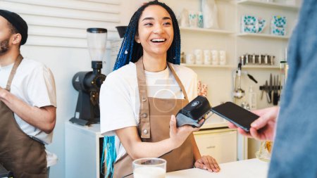 Happy female barista using credit card swipe machine. Man using mobile phone while making payment in coffee shop. Electronic money. Mobile banking