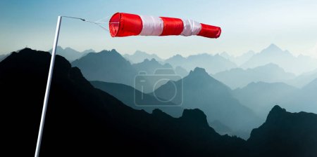 Photo for Windsack with red stripes and blue mountain ranges silhouette in early Morning Sunlight. Concept for Prediction and Vision for new and creative business solutions. Alps, Allgau, Bavaria, Germany. - Royalty Free Image