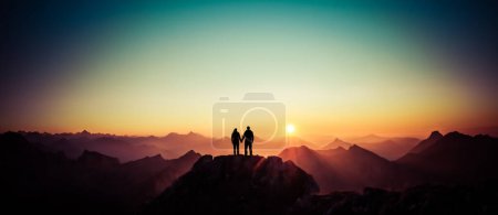 Foto de Happy winning success man and woman at sunset or sunrise standing on mountain peak holding hands and are happy for having reached mountain top summit goal during hiking travel trek. Tirol, Austria - Imagen libre de derechos
