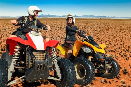 Foto de Happy couple of quad bikers laughing joyful, cheerful and fresh. Young active caucasian couple in outdoor activity driving quad ATV in Namib desert, Namibia, Africa. - Imagen libre de derechos