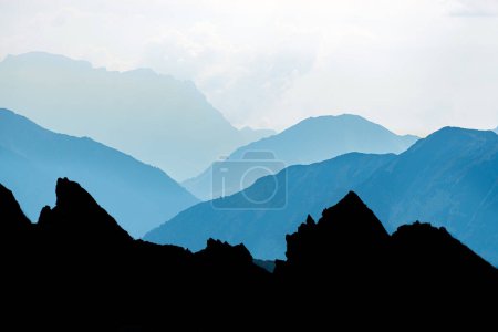 Foto de Blue and cyan mountain peaks silhouette with bright backlight during sunrise. Alps, Tirol, Austria. - Imagen libre de derechos