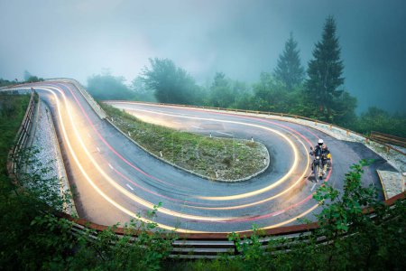 Foto de Motorcycle driving through Hairpin curve mountain road with beautiful light trails and streaks. High Risk driving conditions with fog, slippery surface and low visibility. Alps, Slovenia. - Imagen libre de derechos