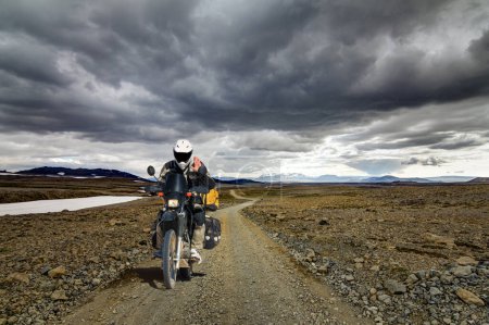 Foto de Lonely Motorbiker Man drives through icelandic Highland Landscape with Motorcycle and Travel Equipment on dirt road F550 in Kaldidalur, Iceland. - Imagen libre de derechos
