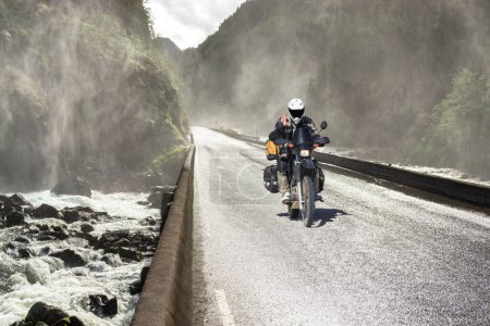 Foto de Moto de conducción rápida en la carretera del valle del cañón húmedo y el puente sobre el río. Condiciones de conducción difíciles. Países Bajos. - Imagen libre de derechos