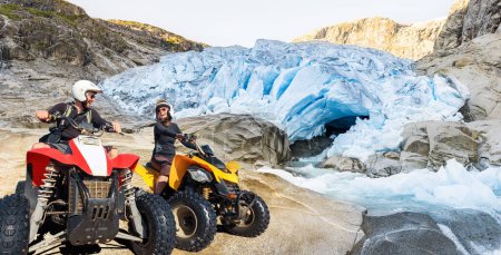 Foto de Felices parejas de quads de ATV riendo alegres, alegres en el paisaje ártico glaciar. Pareja joven activa en actividad al aire libre conduciendo quadbikes. - Imagen libre de derechos
