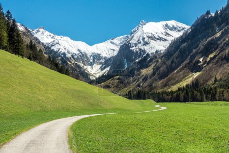 Foto de Increíble paisaje con montañas nevadas, verdes prados de hierba y sinuosas rutas de senderismo en primavera. Alpes, Trettachtal, Allgaeu, Baviera, Alemania. - Imagen libre de derechos