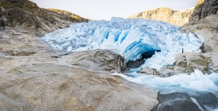Foto de Un hombre parado frente al gran Glaciar Tongue y derretir el río de agua. Vista panorámica de Nigardsbreen, Parque Nacional Jostedalsbreen, Noruega. - Imagen libre de derechos
