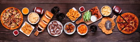 Foto de Superbowl or football theme food table scene. Pizza, hamburgers, wings, snacks and sides. Above view on a dark wood banner background. - Imagen libre de derechos