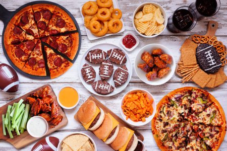 Photo for Super Bowl or football theme food table scene. Pizza, hamburgers, wings, snacks and sides. Above view on a white wood background. - Royalty Free Image