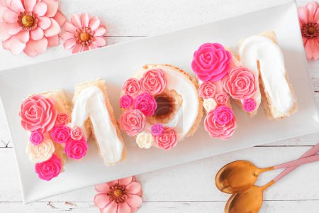 Foto de Día de las Madres Pastel MOM con flores de caramelo rosa y blanco. Escena de mesa vista superior con fondo de madera blanca. - Imagen libre de derechos