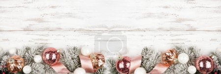Téléchargez les photos : Bordure de fond de Noël de branches enneigées, ruban rose givré et ornements en or rose. Vue ci-dessus sur un fond de bannière en bois blanc. Espace de copie. - en image libre de droit