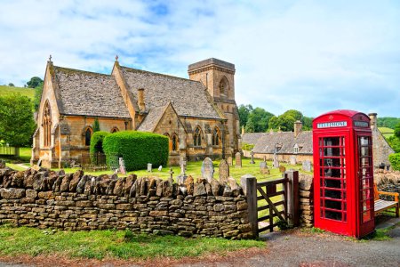 Cotswolds Dorfkirche mit roter englischer Telefonzelle, Gloucestershire, England
