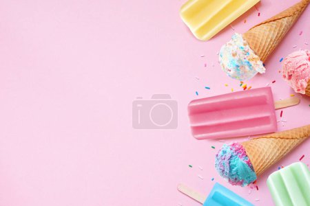 Assorted colorful pastel summer ice cream cones and popsicle frozen desserts. Top down view side border on a pink background. Copy space.
