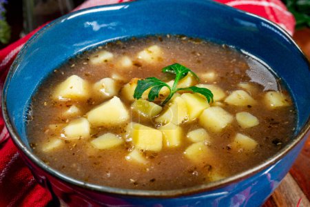Saure Suppe mit Pilzen serviert mit Kartoffeln in blauer Schüssel.
