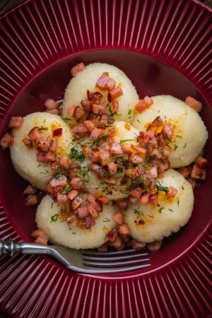 Kartoffelknödel mit Speck, Zwiebeln und Schinken auf einem Teller.